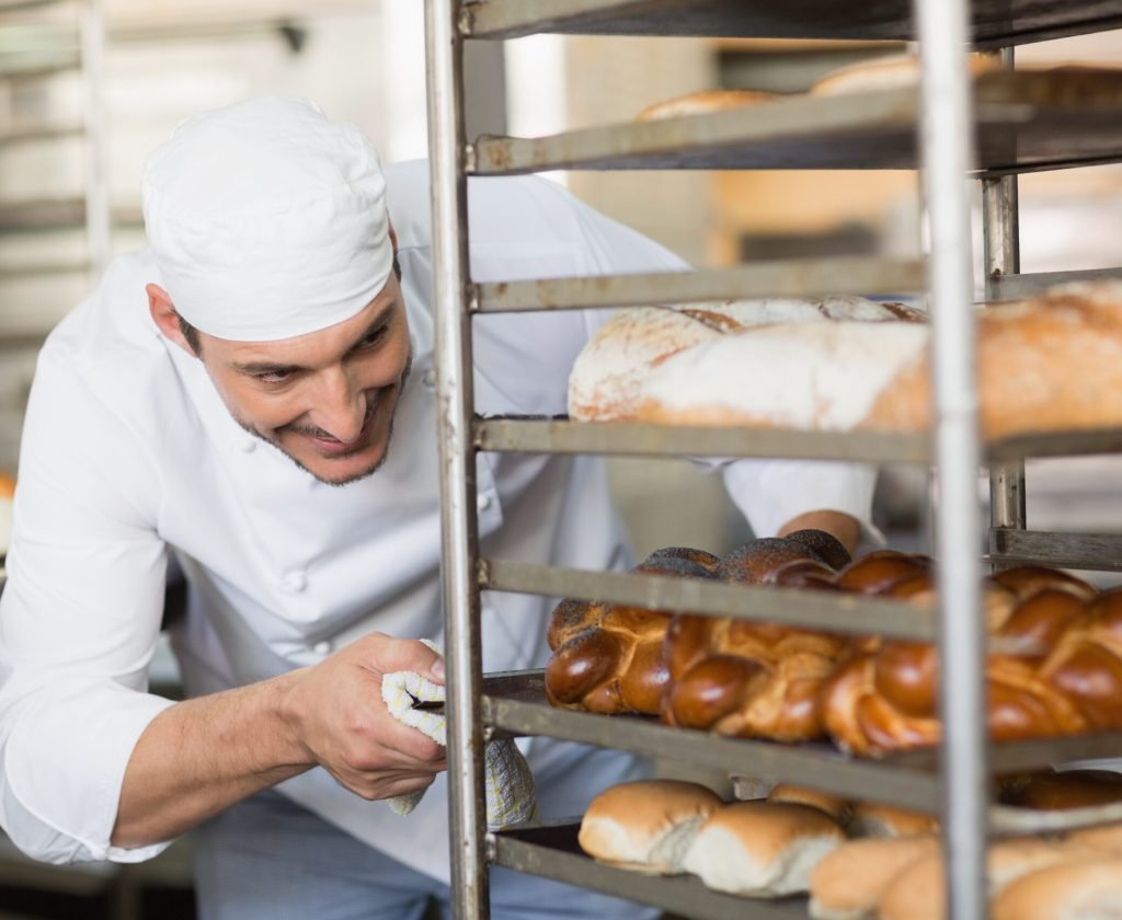 Smiling baker pushing tray of bread in the kitchen of the bakery